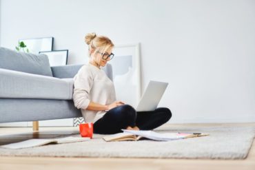A woman types on a laptop in front of her couch.