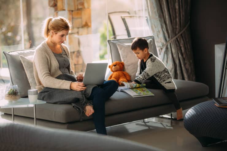 A woman works on a couch while a child plays.