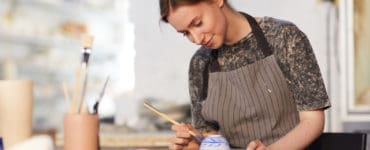 A woman paints a ceramic bowl.